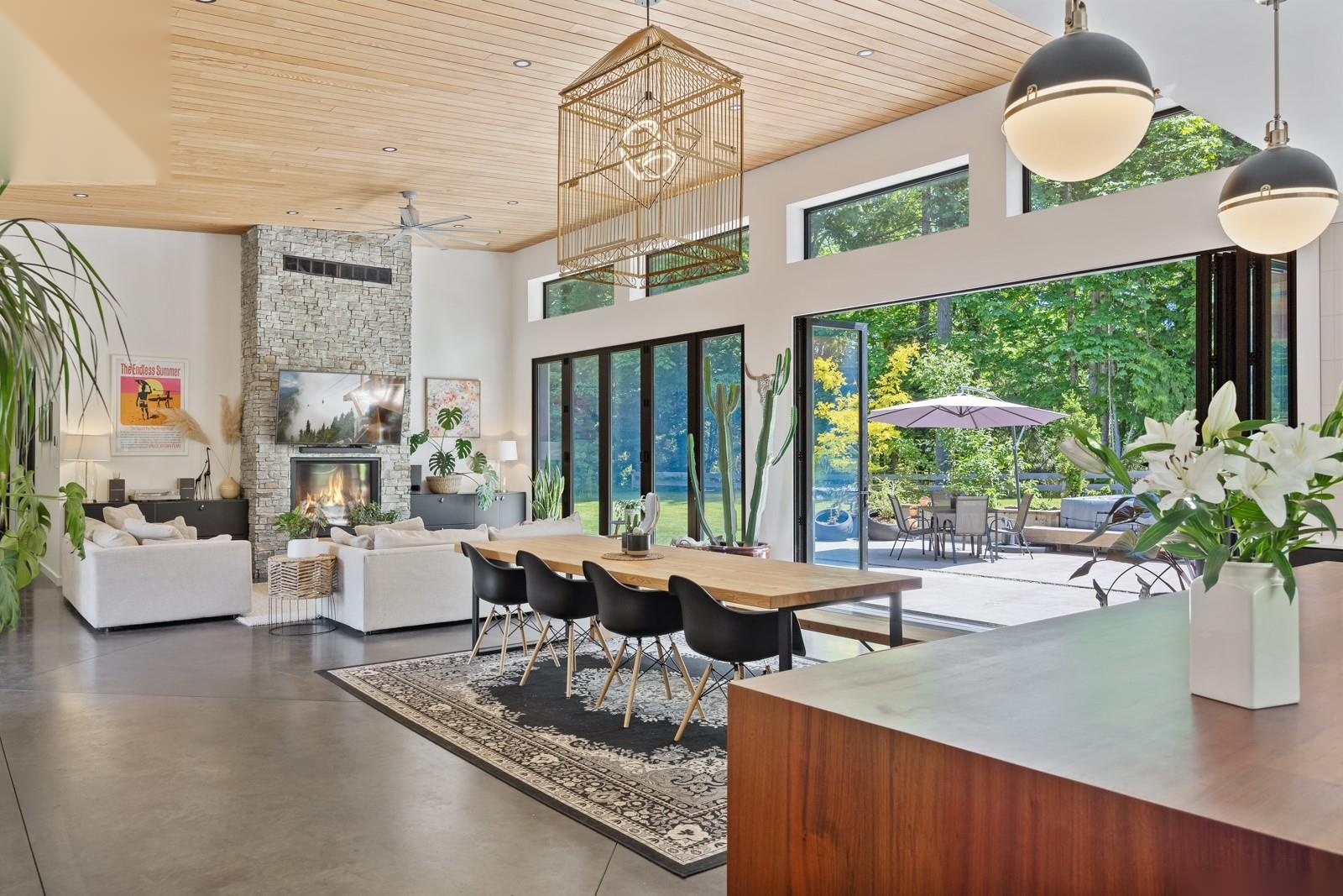 Open concept Casero living room with wood ceiling, stone fireplace, and walls of glass