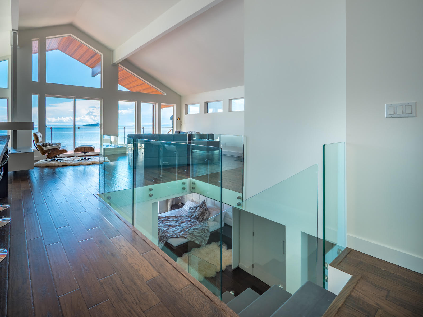 Upper landing with glass railings overlooking the ocean and vaulted ceilings